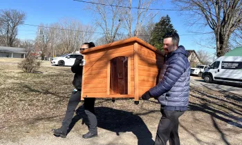 Two people carrying a doghouse