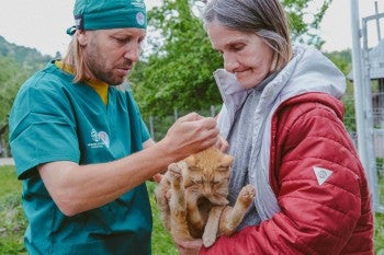 A woman holds a cat while a vet checks them over