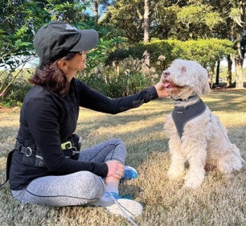 Woman sits on grass, petting a dog.