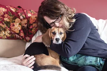 Teddy and his adopter cuddling on a couch