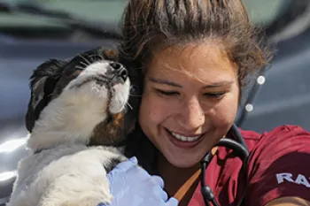 a RAVS volunteer laughs while the small dog she's holding nuzzles her face