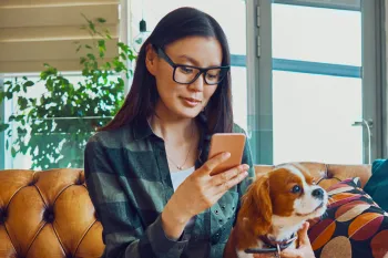 Woman sitting on couch with dog using her phone 