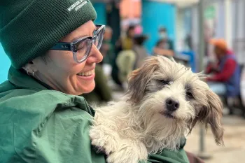 A dog is held by a smiling person in a green hat and jacket.