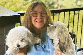 Woman sitting on a deck holding her two white dogs.