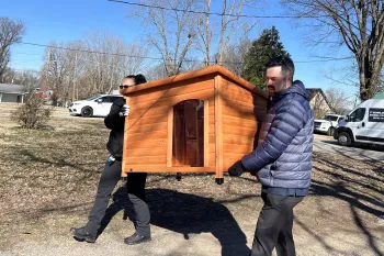 Two people carrying a doghouse