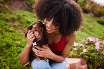 Smiling young woman sitting with her cute little dachshund outside
