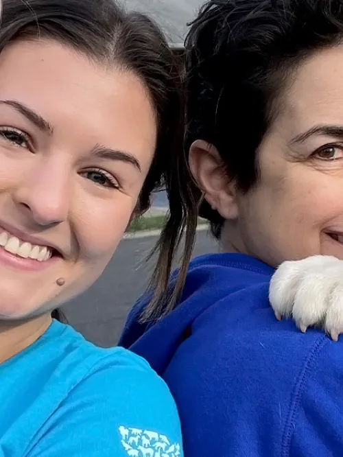 Two women are holding puppies and smiling at the camera