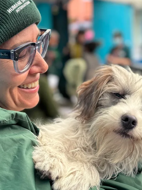 A dog is held by a smiling person in a green hat and jacket.