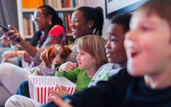 Multi-ethnic family watching movie and eating popcorn on the couch watching a movie with a dog.